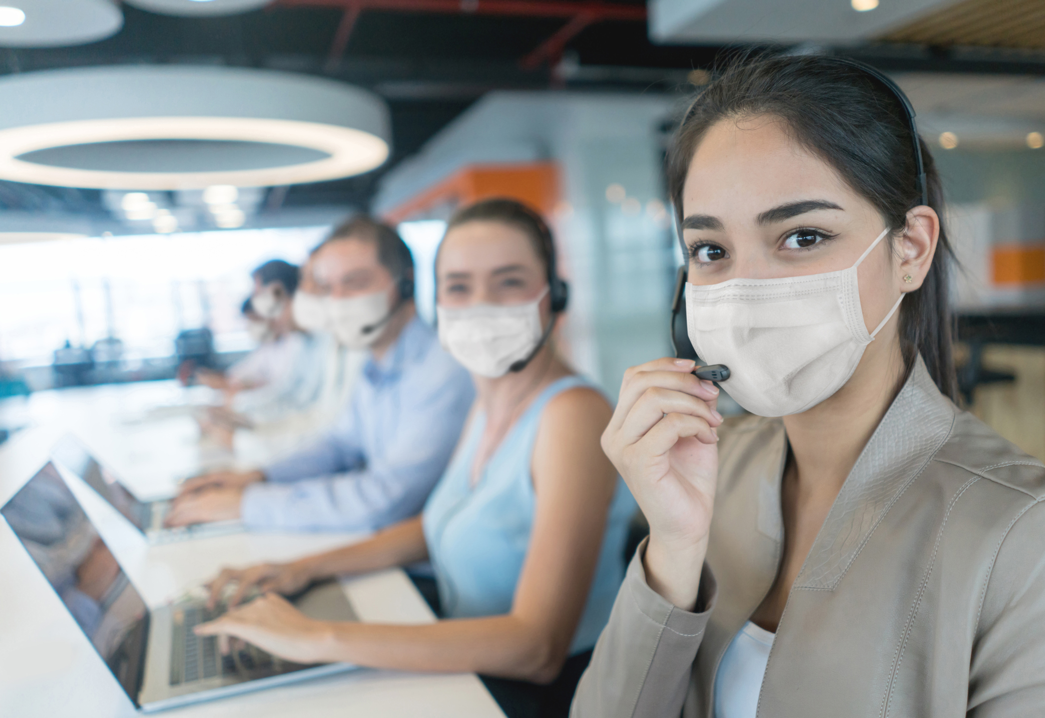 Group of customer service representatives working at a call center wearing facemasks during the COVID-19 pandemic